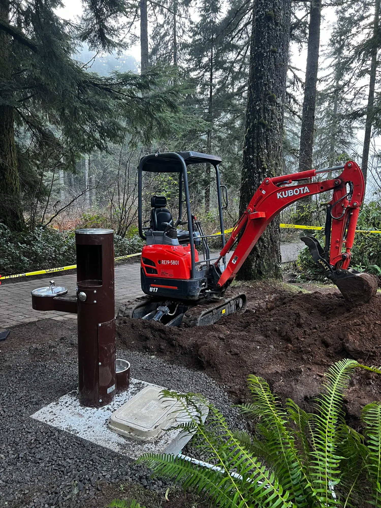 Excavator installing new water fountain near forest trail