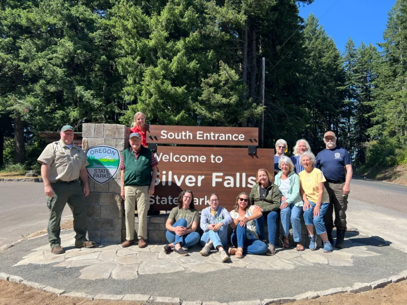 Group of volunteers gathered beside Silver Falls State Park south entrance welcome sign in Oregon