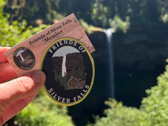 Friends of Silver Falls membership patch and pin displayed beside South Falls waterfall