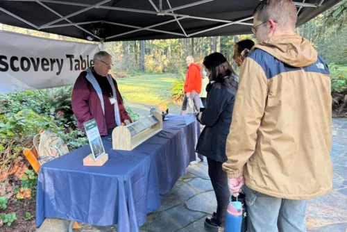 jan at Table Park ranger hosts outdoor Discovery Table booth under tent, greeting visitors in forested park setting with stone patio.