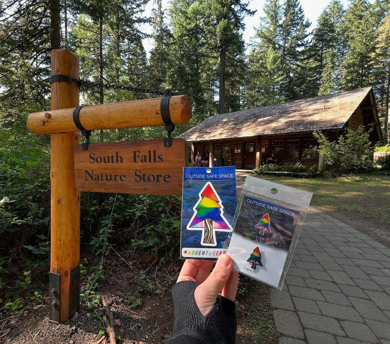 South Falls Nature Store featuring an “Outside Safe Space” pride sticker and pin display in front of the rustic lodge-style building
