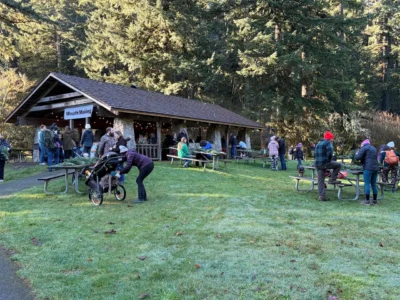 Families and visitors gathering for a festive winter wreath-making event at a rustic forest shelter